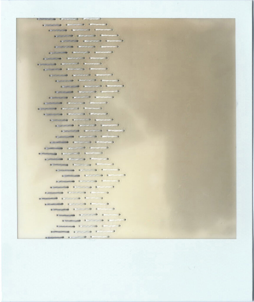 An undeveloped polaroid that has been stitched down the left hand side using a traditional blackwork embroidery pattern. The stitching is done in gradients of grey. The pattern consists of rows of staggered straight lines that give the overall impression of a column of zig zags.